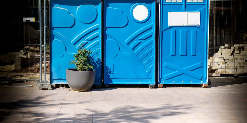 Blue portable toilets with hand wash station and exterior lighting at outdoor event
